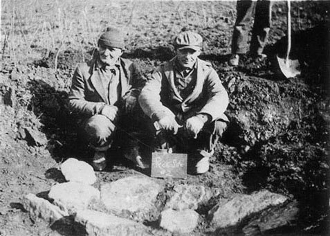Two members of field crew at Peck 2 sit near a rock-covered pit.